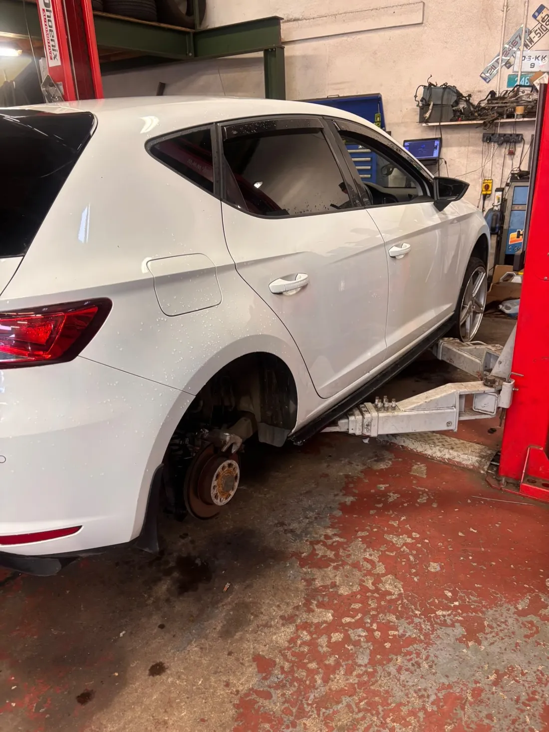 White hatchback raised on a workshop lift with a rear wheel removed for brake work